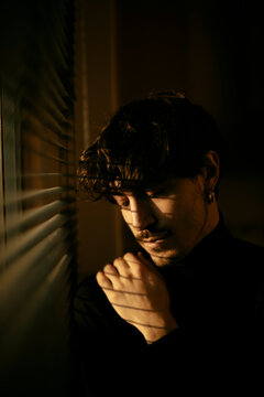 Thoughtful young man in dramatic indoor window light and shadow