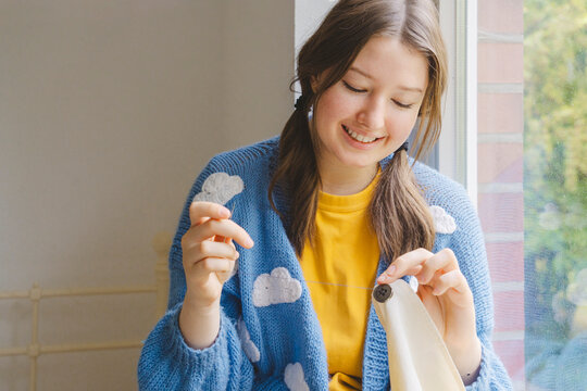 Smiling teenage girl sewing button on clothing