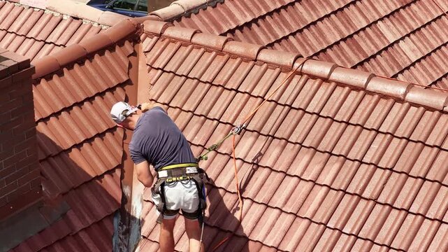 Roof renovation process with spray painting of roof tiles, including priming and applying second coat of paint on a residential roof, showing professional exterior maintenance and refurbishment work.