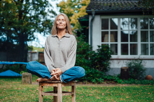Woman practicing yoga on stool at backyard