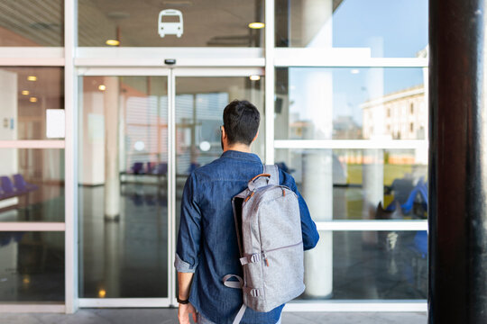 Back view of man with backpack in front of entrance of bus station