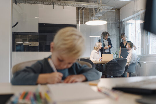 Boy painting in office with business team having a meeting