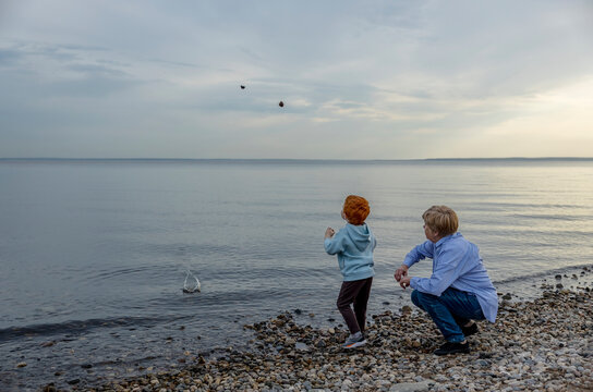 Grandmother with grandson throwing pebbles in sea at beach