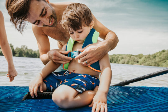 Father fastening life jacket for son in lake