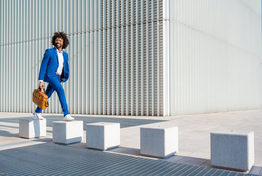 Happy businessman holding shoulder bag walking on concrete block