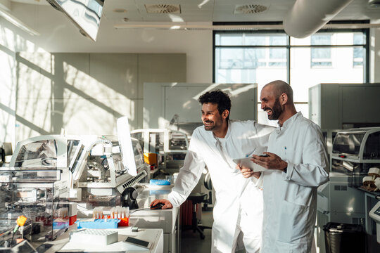 Smiling scientist colleagues working at monitor in bright laboratory