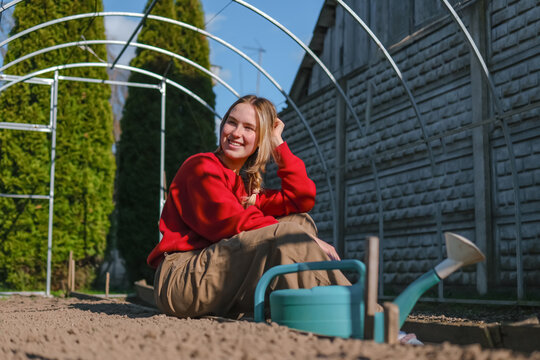 Smiling woman resting in backyard greenhouse with watering can