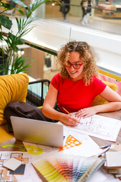 Smiling female architect drawing on blueprint at desk
