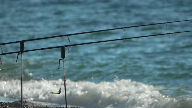 Fishing ocean angler, rods waiting patiently for a bite set up on the seashore against sparkling blue waves.