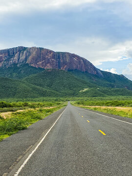 Long straight road traversing Kenyan savanna with mountains