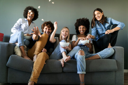 Exuberant friends sitting on couch throwing popcorn