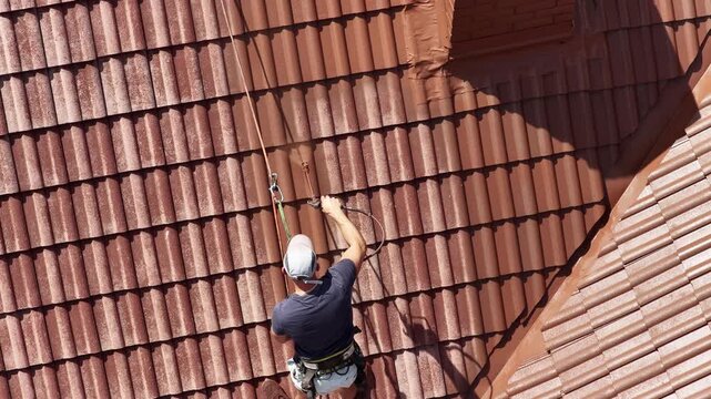 Roof renovation process with spray painting of roof tiles, including priming and applying second coat of paint on a residential roof, showing professional exterior maintenance and refurbishment work.