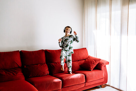 Happy boy listening to music through headphones while dancing on sofa at home