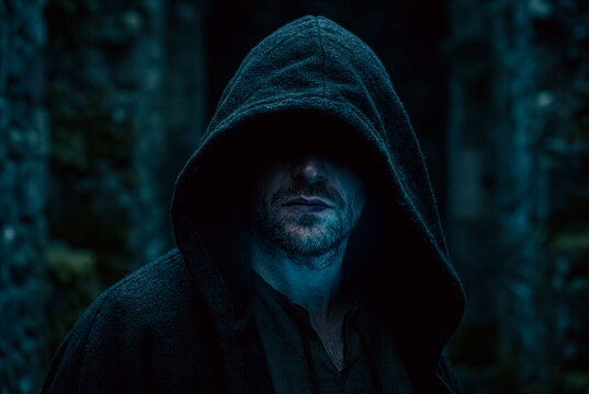 Cinematic portrait of an enigmatic and mysterious man wearing a dark fabric hood that casts a deep shadow over his face.