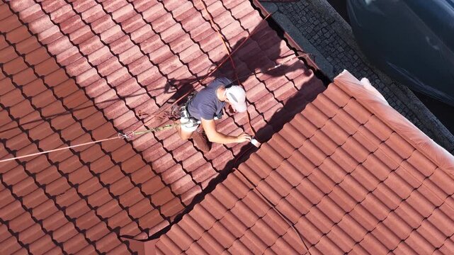 Roof renovation process with spray painting of roof tiles, including priming and applying second coat of paint on a residential roof, showing professional exterior maintenance and refurbishment work.