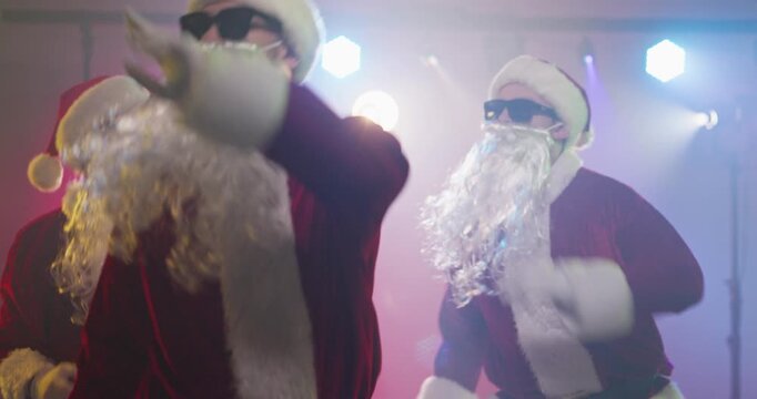 Santa claus dancers dance at christmas party. Energetic group in red costumes moves to disco beats with gifts, neon lights, and festive vibe. Cheerful festive holiday dance party concept.