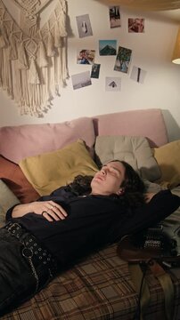 Vertical video of young man lying on bed with eyes closed, resting next to electric guitar. Perfect for illustrating youth lifestyle, mental health, or creative burnout concepts