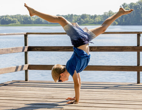 Athletic little boy doing a handstand on a wooden pier by the river.