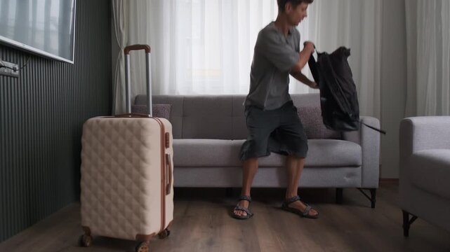 Digital nomad arrival and remote work lifestyle. Man entering apartment with luggage, unpacking laptop and starting work immediately