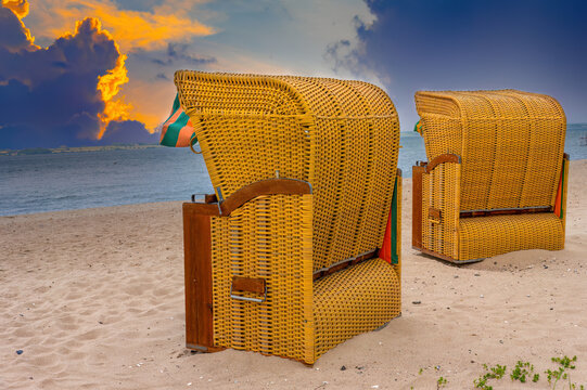 Beach chairs on a sandy beach under dramatic storm clouds at sunset
