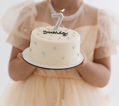 Seven year old girl holding birthday cake with silver number candle