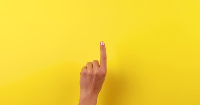 Close-up video of a woman&rsquo;s hand pointing with her index finger on a bright yellow background. Minimal motion gesture concept symbolizing direction, choice, attention, instruction, and communication.