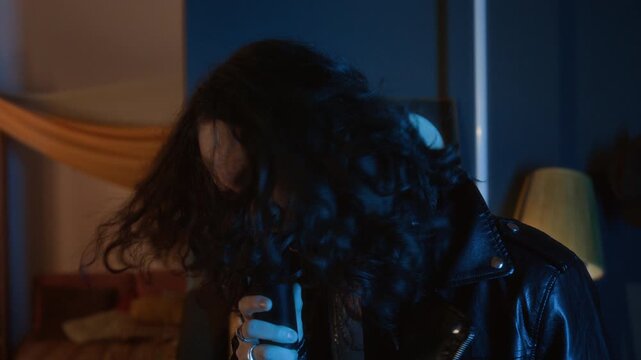Young musician with long hair wearing leather jacket singing passionately into microphone and headbanging. Clip for music industry promos or youth lifestyle commercials