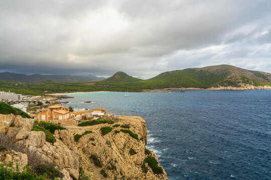 Elevated view of Cala Agulla Beach in Mallorca, Spain, with turquoise Mediterranean waters, sandy shoreline, seaside hotels. Scenic coastal landscape, summer vacation, travel destination.