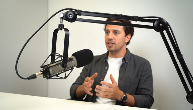 Young adult man speaking into a professional studio microphone during a podcast recording, male host or guest sharing ideas for digital broadcast and media production