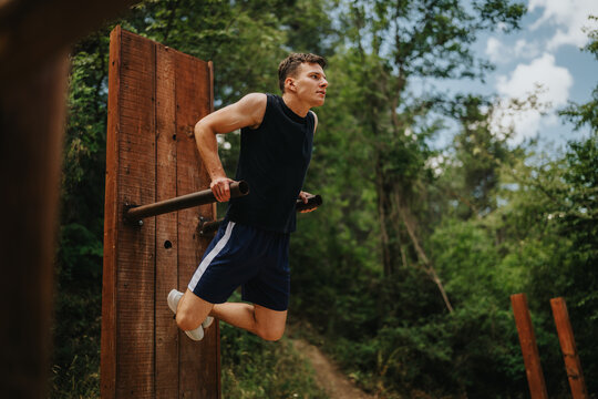 Male athlete performs dips on wooden parallel bars outdoors for upper-body strength. Outdoor workout in a forest setting showing focused calisthenics training.