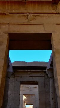Kom Ombo temple columns with composite capitals and hieroglyphic carvings viewed from below against blue sky in Egypt, upward perspective of ancient sandstone architecture