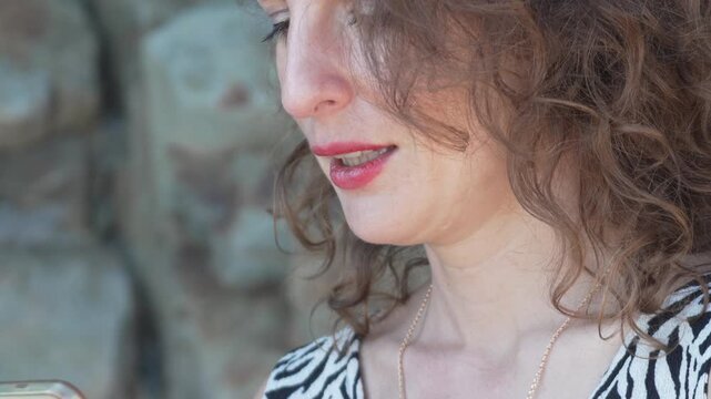 Woman smartphone talking close up of a woman speaking while looking at her mobile phone near a stone wall outdoors