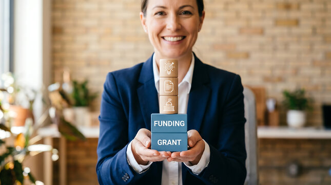 Smiling professional woman holds a stack of wooden blocks featuring funding and grant concept icons