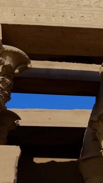Kom Ombo temple columns with composite capitals and hieroglyphic carvings viewed from below against blue sky in Egypt, upward perspective of ancient sandstone architecture