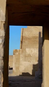 Kom Ombo temple columns with composite capitals and hieroglyphic carvings viewed from below against blue sky in Egypt, upward perspective of ancient sandstone architecture