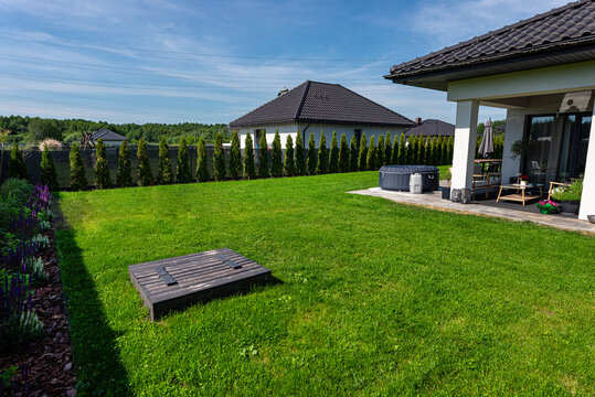 Private garden with lush green lawn, hot tub, and modern house