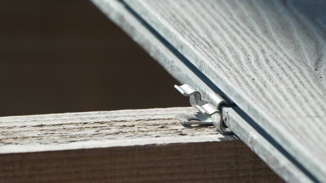 Woodworking construction carpentry hands installing decking board with metal fasteners on outdoor frame to build modern patio project in backyard