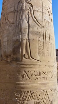 Kom Ombo temple columns with composite capitals and hieroglyphic carvings viewed from below against blue sky in Egypt, upward perspective of ancient sandstone architecture