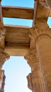Kom Ombo temple columns with composite capitals and hieroglyphic carvings viewed from below against blue sky in Egypt, upward perspective of ancient sandstone architecture