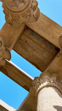 Kom Ombo temple columns with composite capitals and hieroglyphic carvings viewed from below against blue sky in Egypt, upward perspective of ancient sandstone architecture