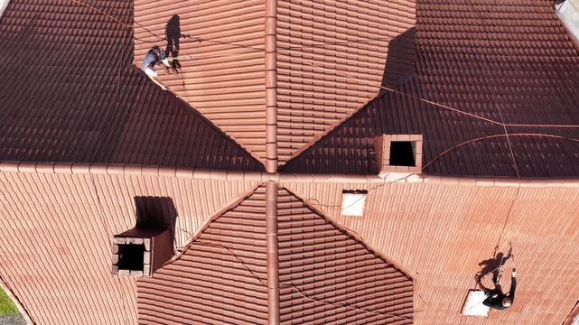 Roof renovation process with spray painting of roof tiles, including priming and applying second coat of paint on a residential roof, showing professional exterior maintenance and refurbishment work.