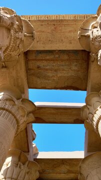 Kom Ombo temple columns with composite capitals and hieroglyphic carvings viewed from below against blue sky in Egypt, upward perspective of ancient sandstone architecture