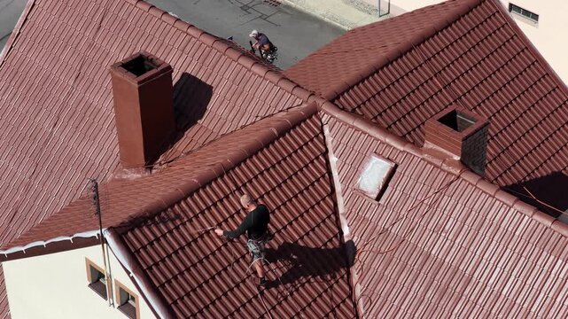 Roof renovation process with spray painting of roof tiles, including priming and applying second coat of paint on a residential roof, showing professional exterior maintenance and refurbishment work.