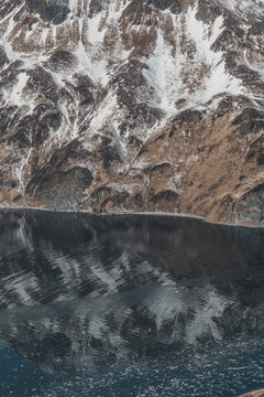 Aerial view of snow-capped mountains and reflective dark waters with floating ice fragments in Unalaska, Alaska, United States.