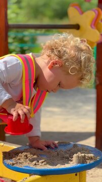 Curly haired child playing with sand and form on playground. Toddler building tower in sandbox. Educational leisure and summer activity for happy little kid.