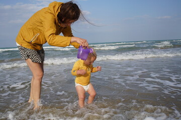 mother pouring water from a watering pot toy onto her toddler's head in the ocean surf © Kamil