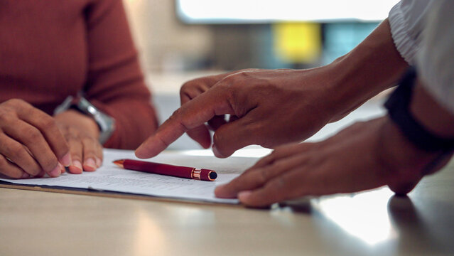 Two hands point at written notes on a table. One hand rests calmly, the other gestures precisely. Red pen lies nearby, suggesting recent work. Focus and collaboration appear evident in the gesture