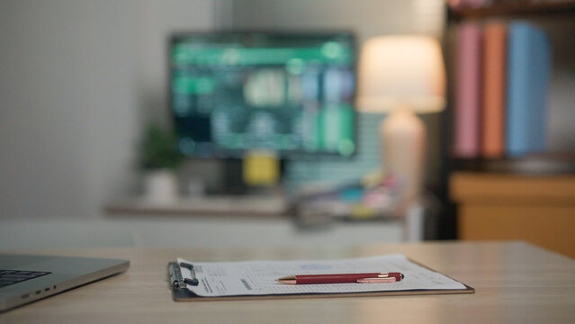 Focused workspace with clipboard and pen on desk. Soft lighting highlights calm, productive atmosphere. Monitor displays data, suggesting analysis or planning. Background features bookshelf and lamp