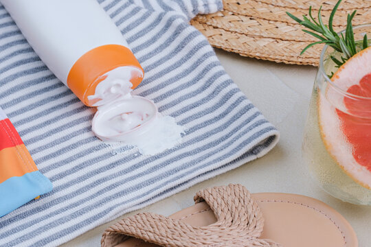 beach scene with sunscreen bottle spilling on sand, top-down perspective, relaxed summery mood, beach accessories, summer products, sun protection, white and orange colors, plastic, textile.