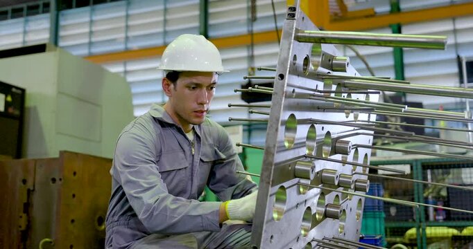 Asian male technician kneels beside metal fixture and checks guide rod alignment, reviewing component position, safety condition, precision setup, maintenance workflow in , slow motion.